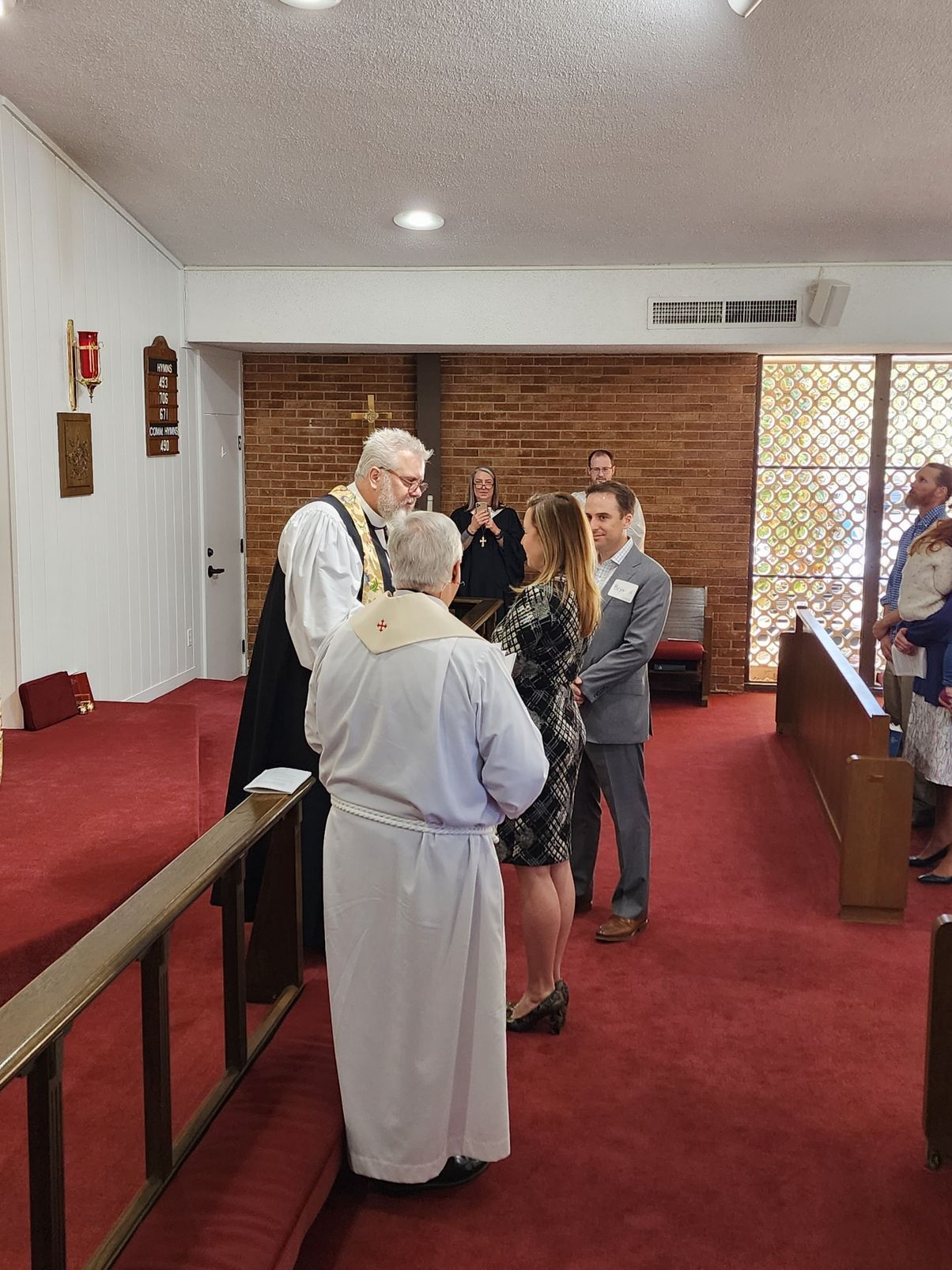 Wedding ceremony in a church: couple with officiant, witnesses and altar on a red carpet.