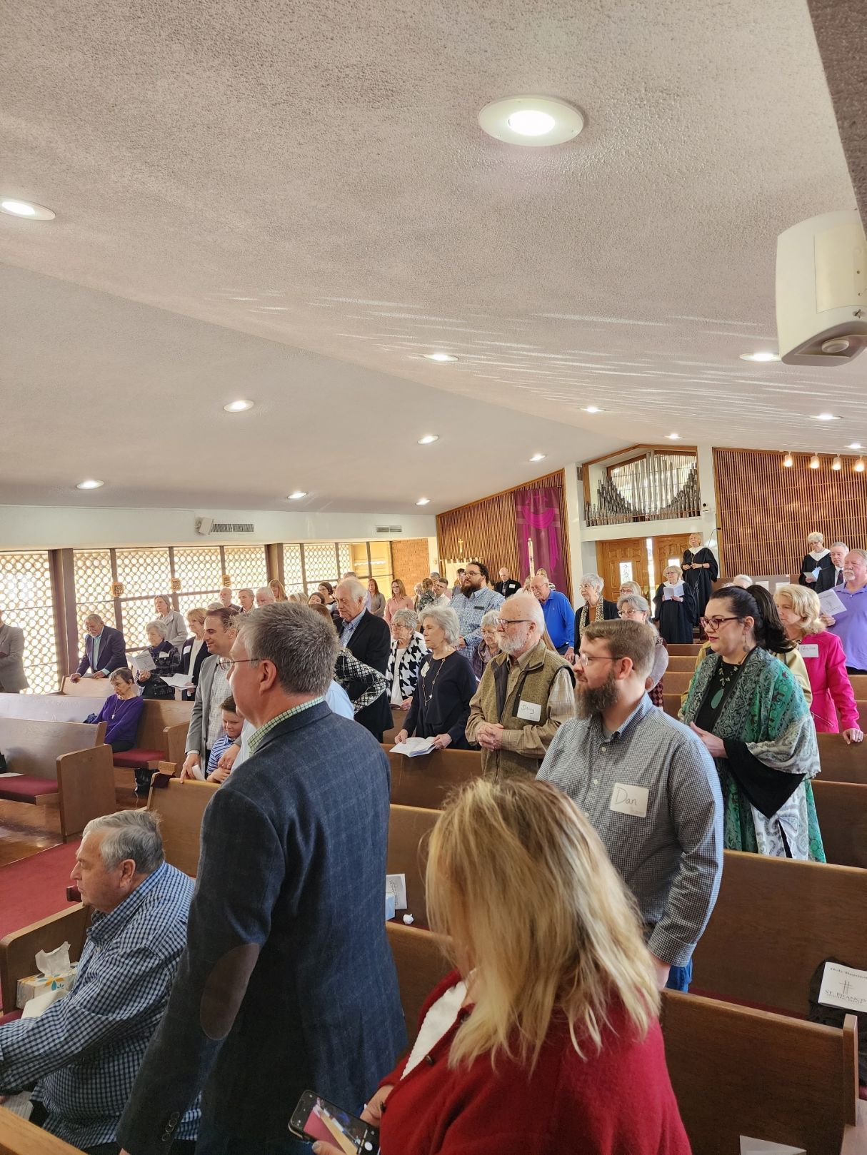 People standing inside a church. Many are looking forward. Light streaming in, warm colors.