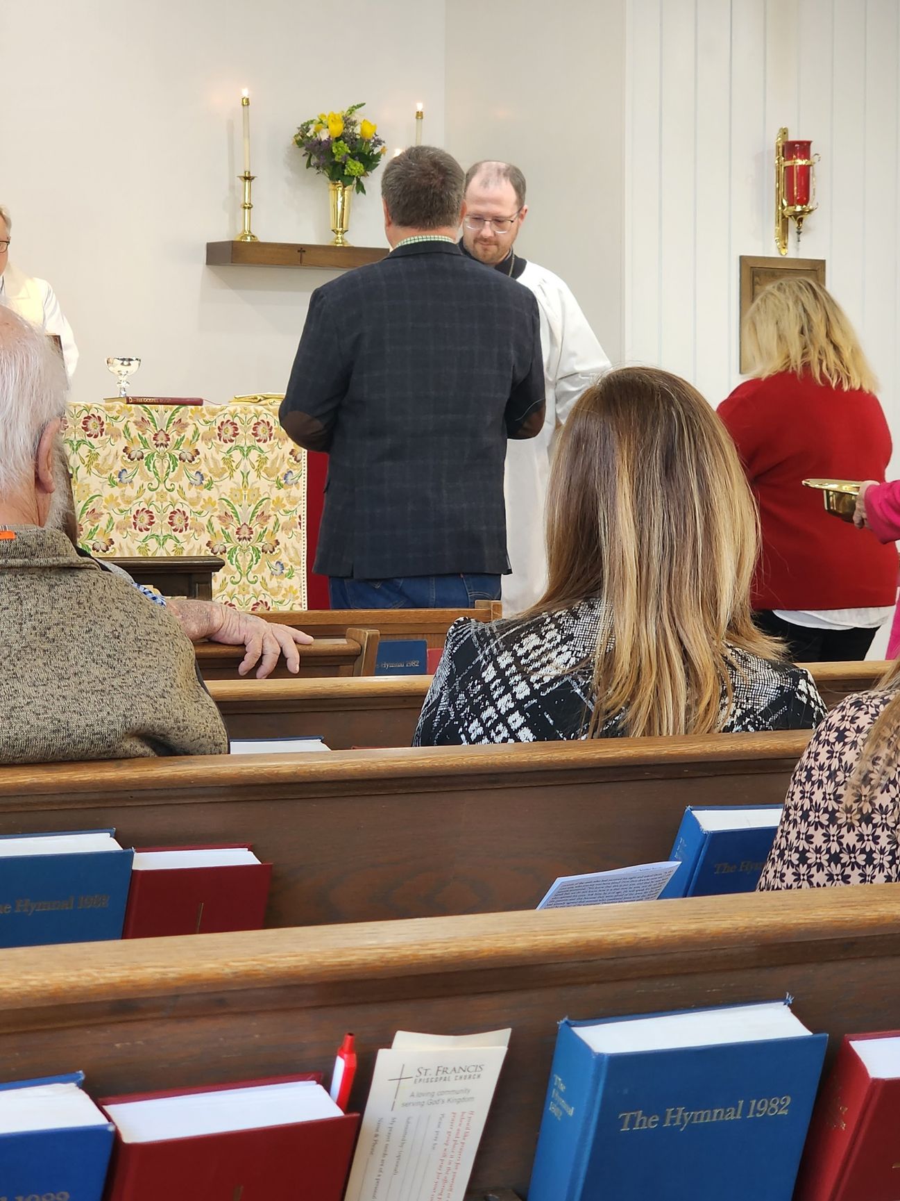 People in a church service; a man is being blessed near the altar.