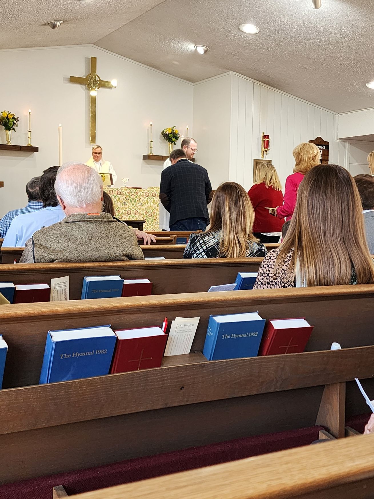 People attending church service, altar with cross, hymn books in pews.