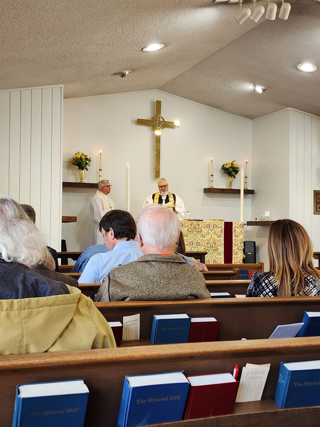 Church service: Priest at altar, people in pews, cross on wall.