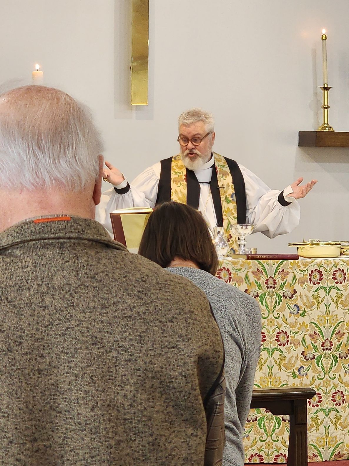 Clergyman at a lectern, hands raised, preaching to people in a church.