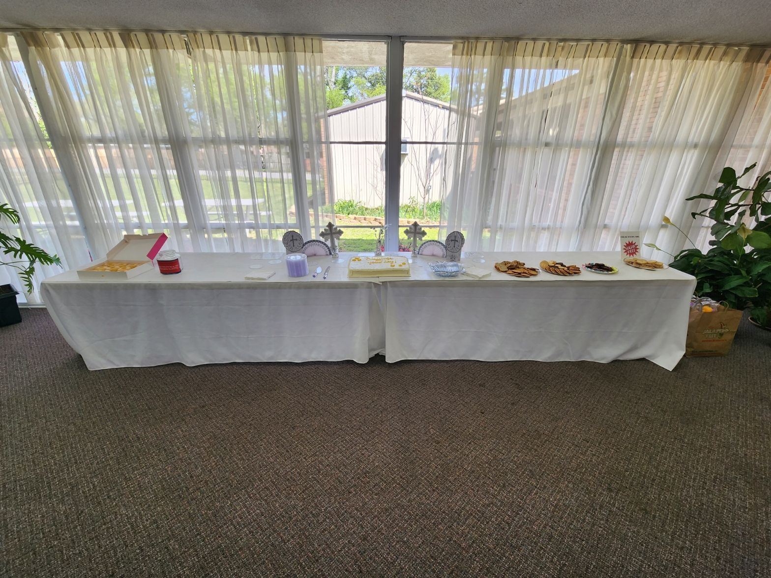 Long table with food, in front of a window with white curtains.