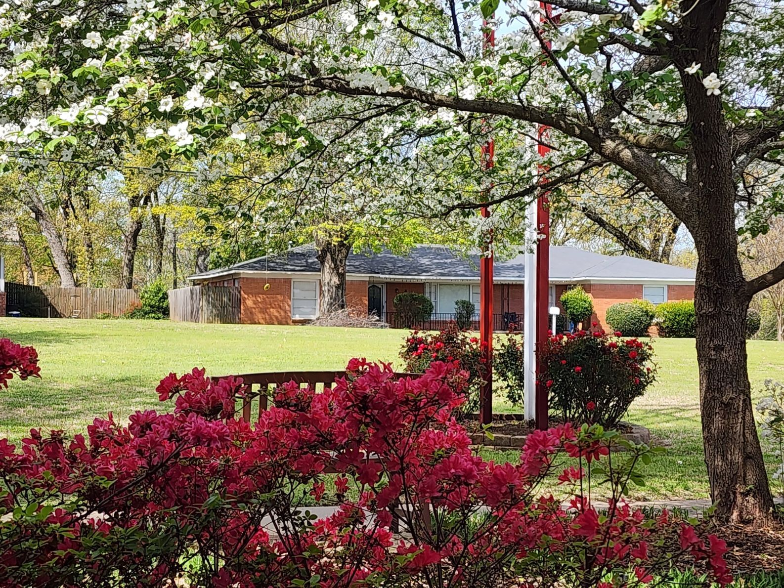 Brick house behind a green lawn with flowering bushes and trees.