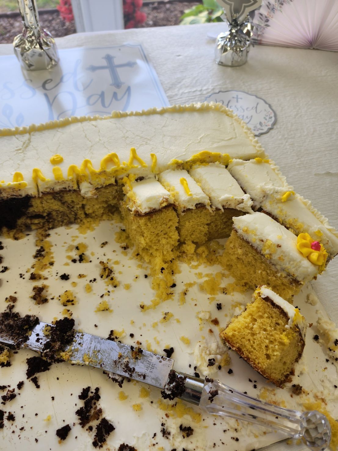Cake on a table, partially eaten. Yellow cake with white frosting and a decorative design.