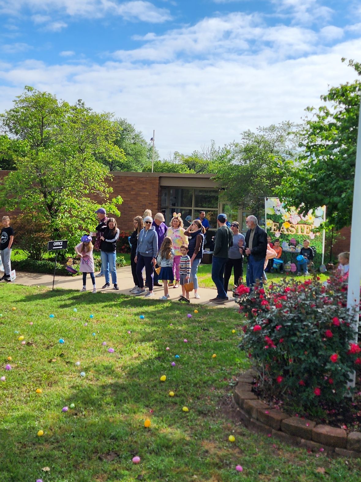 People gathered on a lawn for an Easter egg hunt, eggs scattered on the grass.