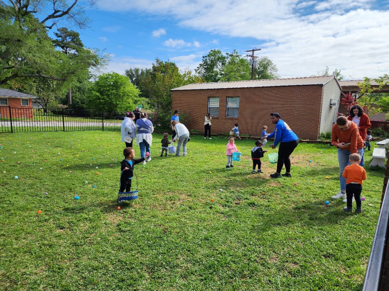 Children and adults collecting Easter eggs in a grassy yard.