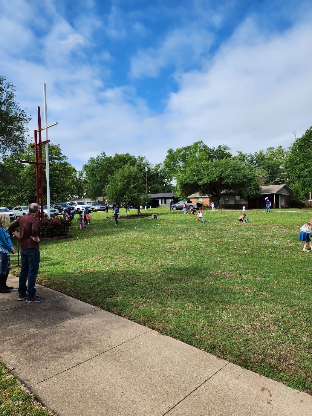 People on a green lawn with a small ship statue, gathering under a blue sky.