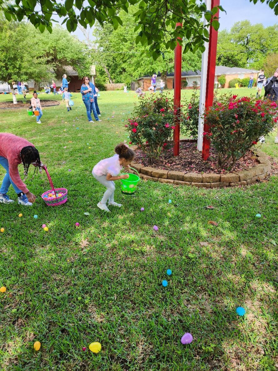 Children gathering colorful eggs on a grassy lawn during an Easter egg hunt.