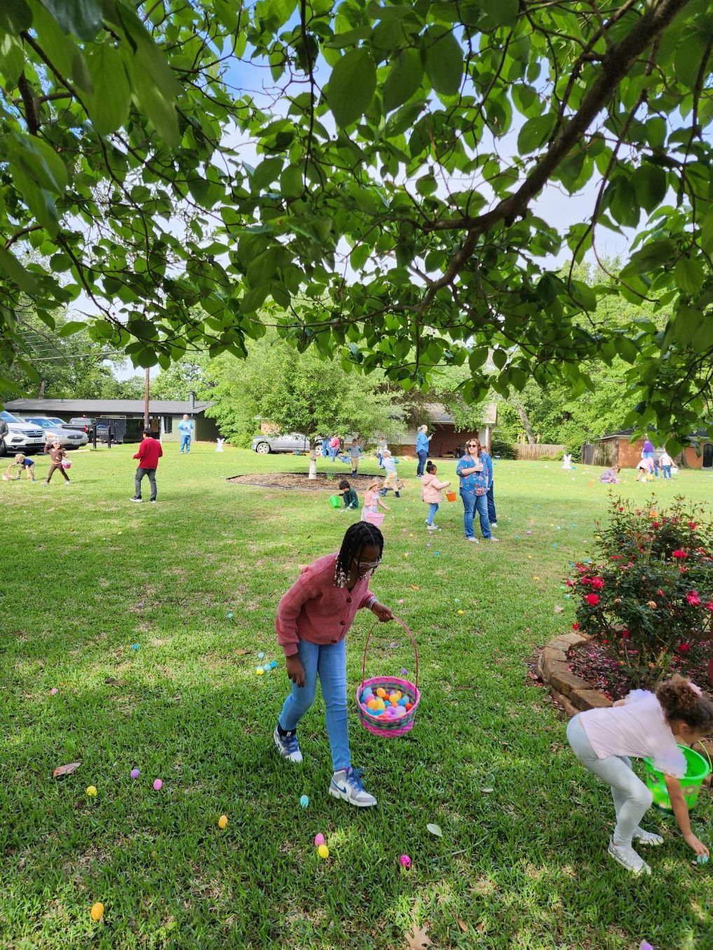 Children hunting for Easter eggs in a grassy yard under a tree.