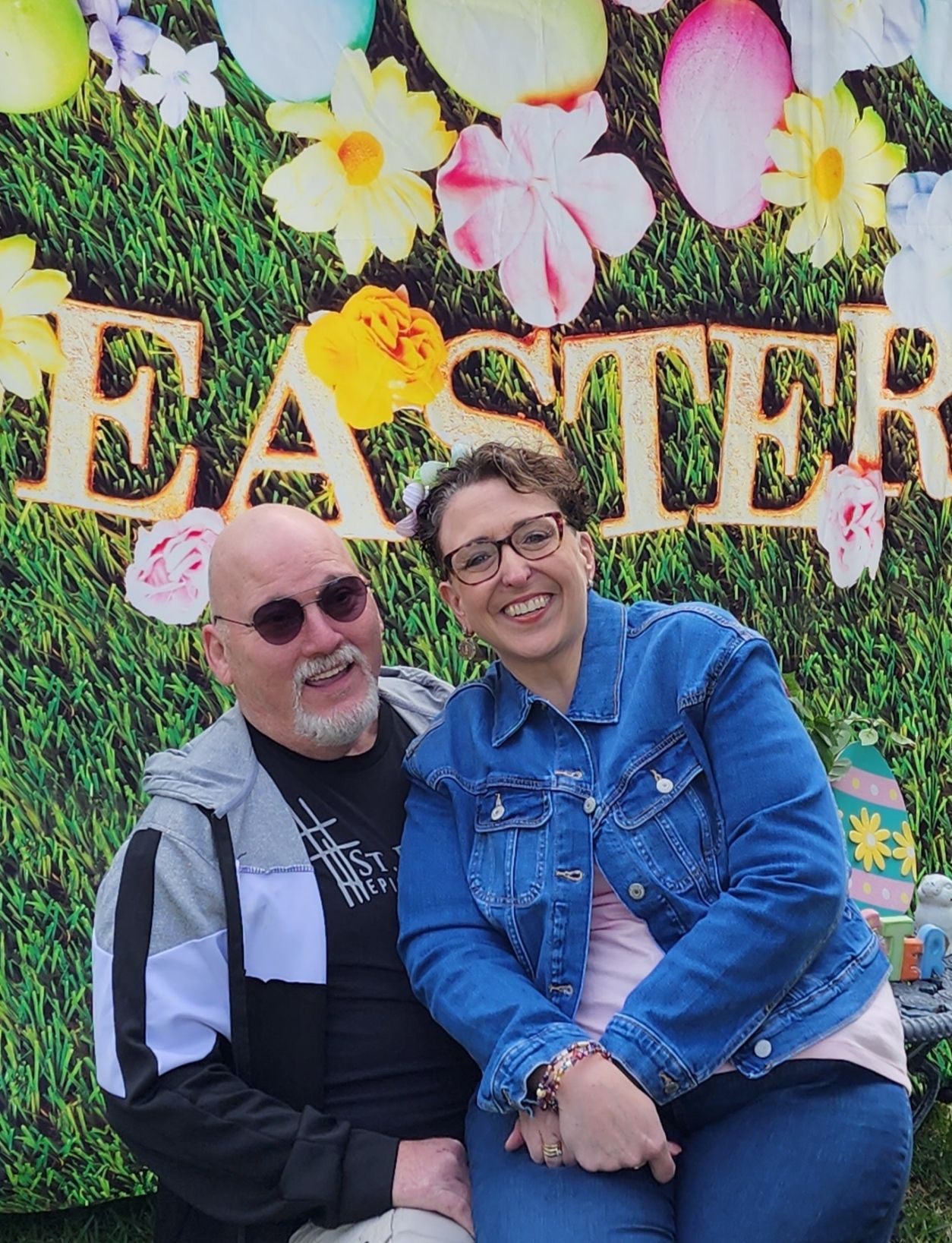 A man and woman smiling in front of an Easter-themed backdrop.