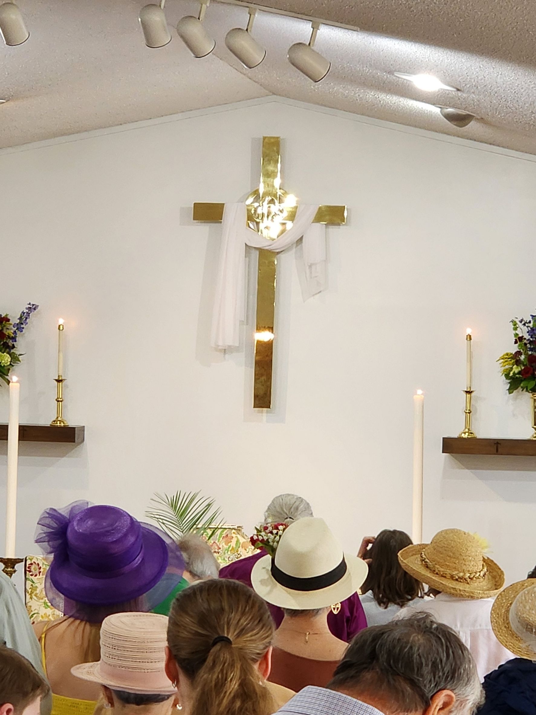Church interior with cross, candles, and people wearing hats.