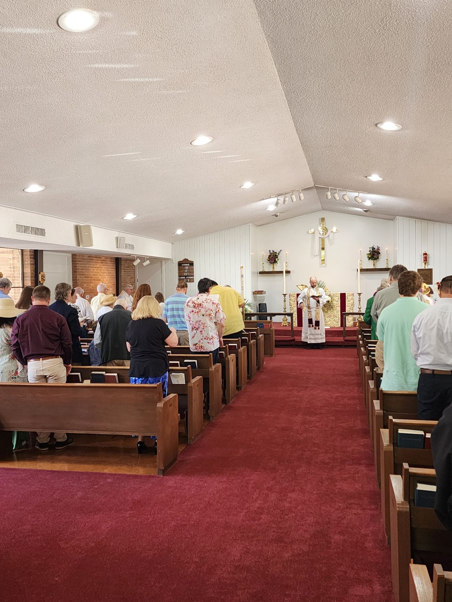 People standing and kneeling in a church during a service, red carpet, priest at altar.