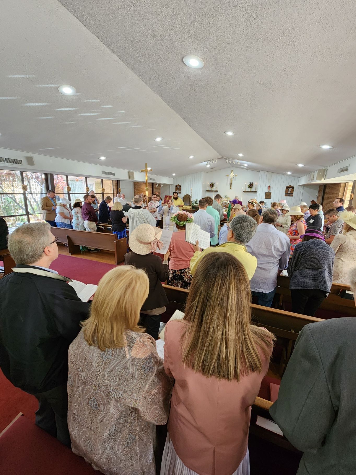 People standing and singing in a church service; natural light from windows.