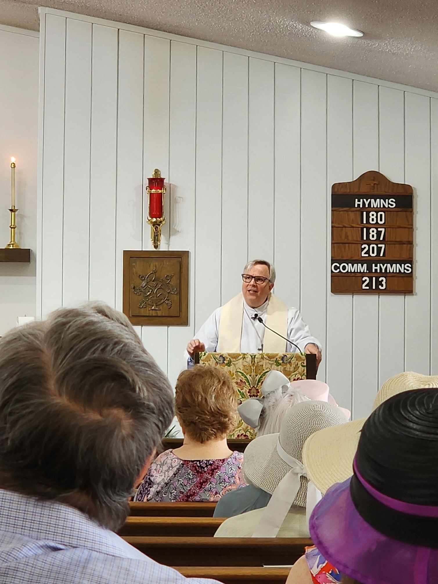 A person in a clerical collar speaking from a podium in a church, facing an audience.