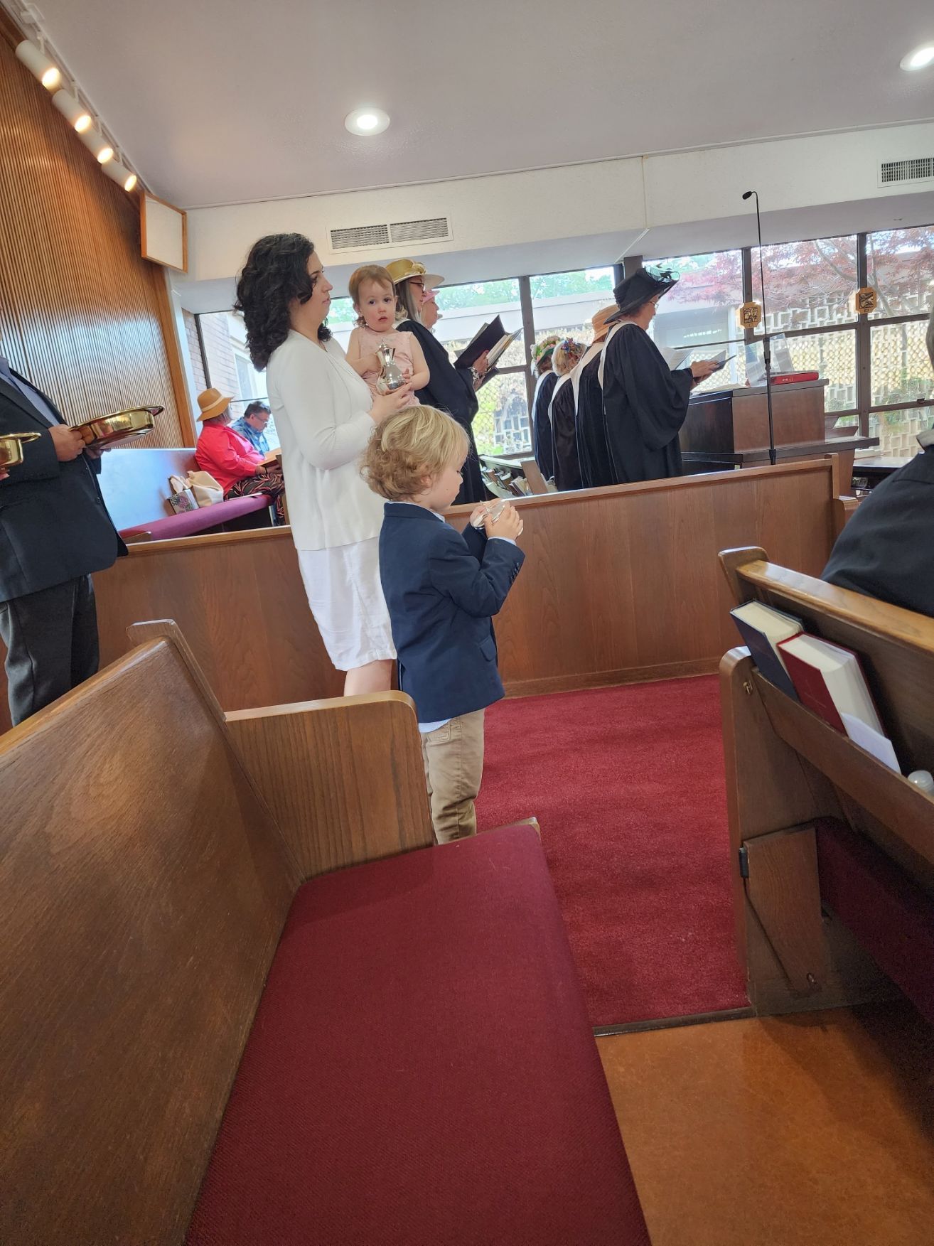 A baptism ceremony in a church. A woman holds a baby, a boy stands nearby; people in robes stand in front.