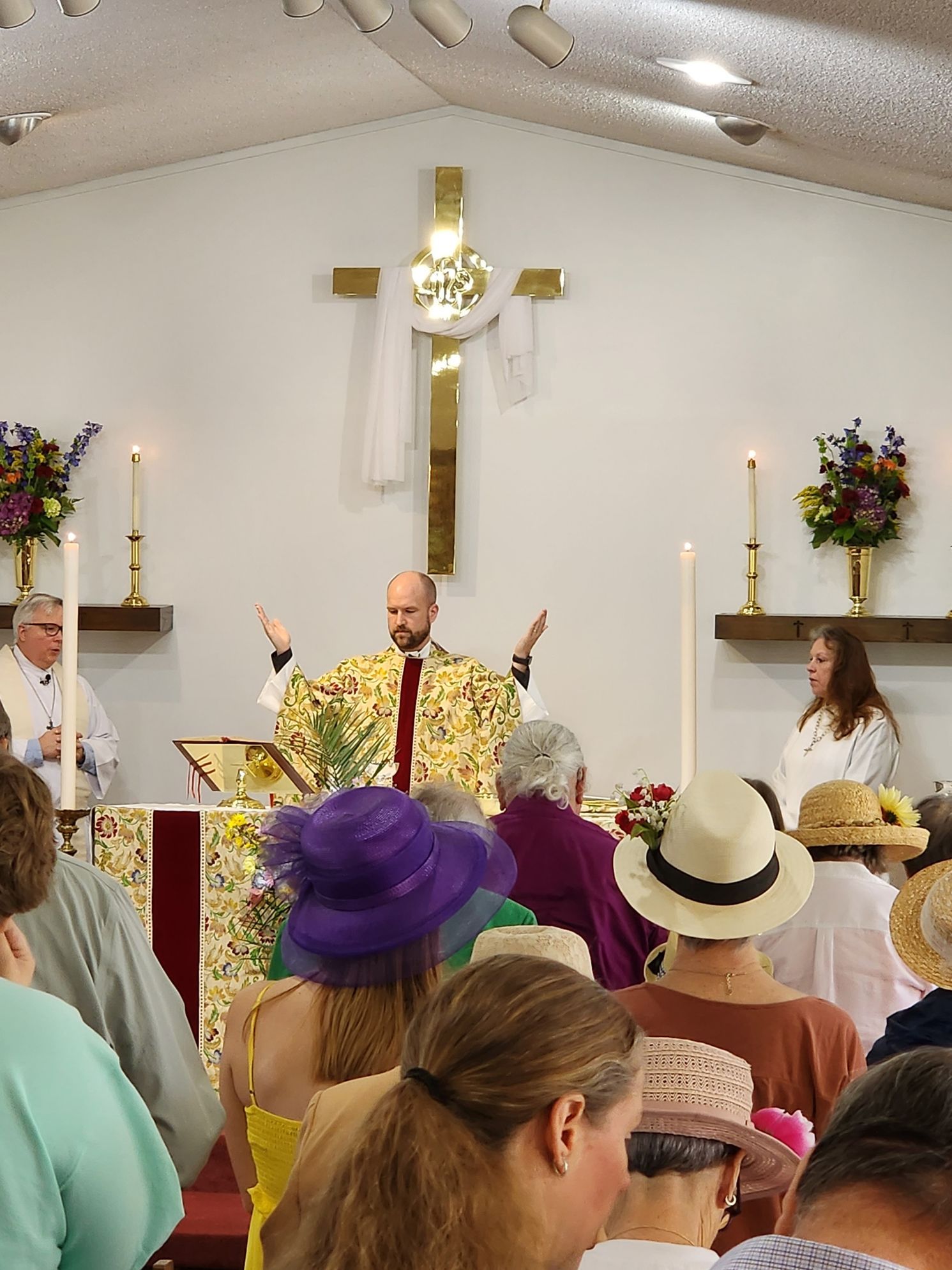A religious ceremony; a priest with raised arms in front of an audience, gold cross, candles.