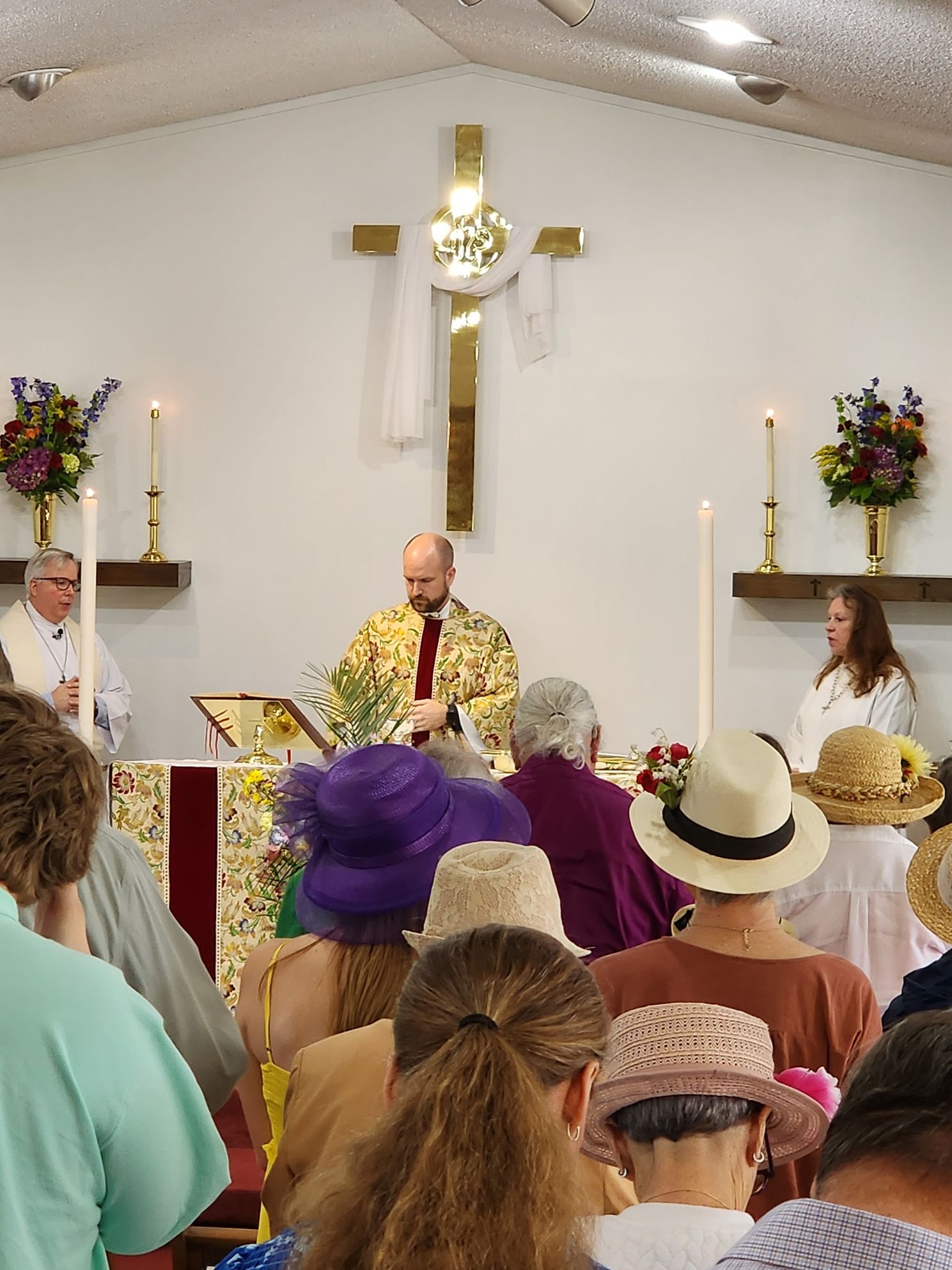 Church service with people facing an altar, a cross, and a priest speaking.