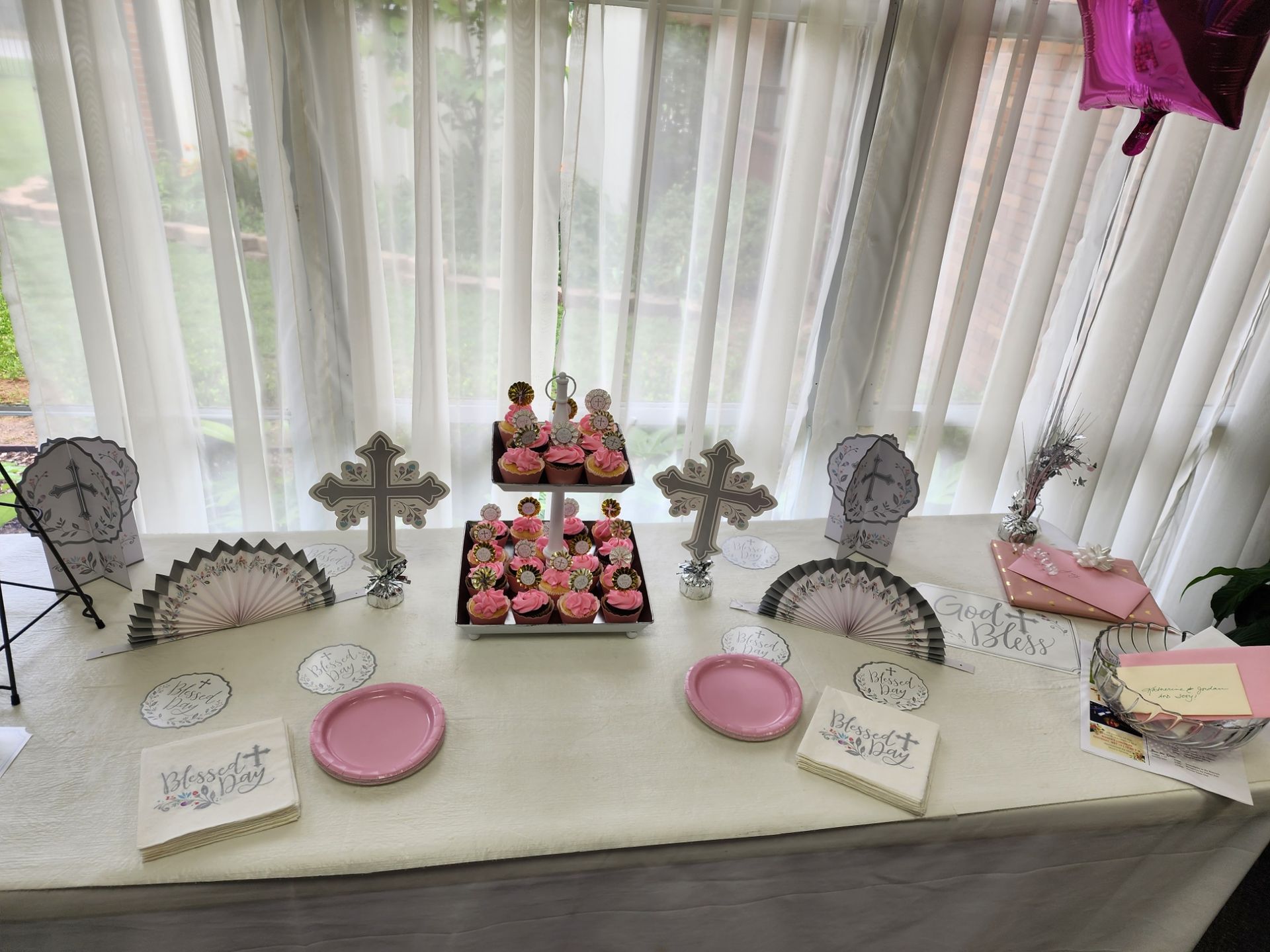 A table set for a celebration. Cupcakes and decorative crosses are visible, along with pink plates and napkins.