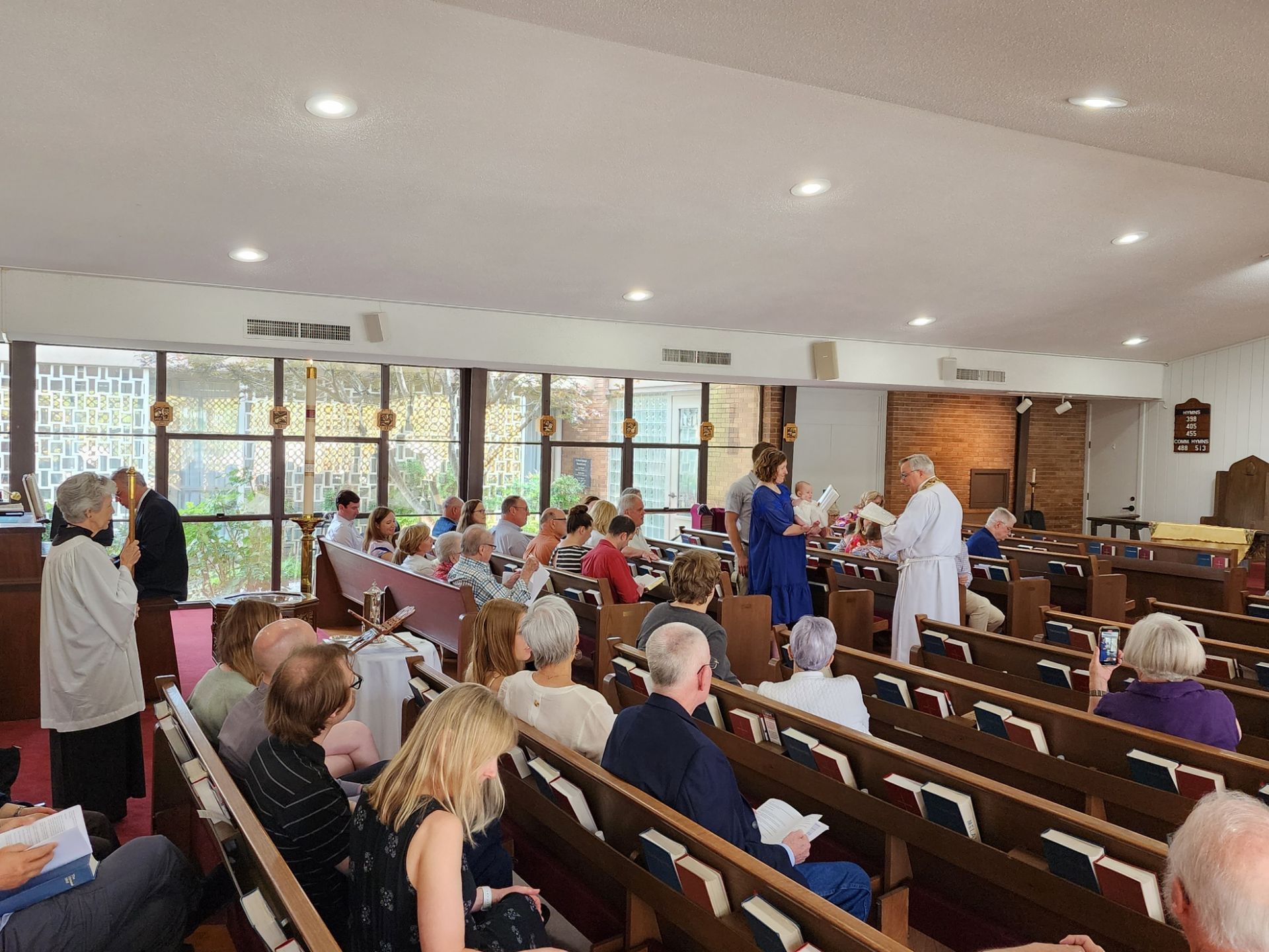 People attending a service in a church. Pews, windows, and religious figures in robes are visible.