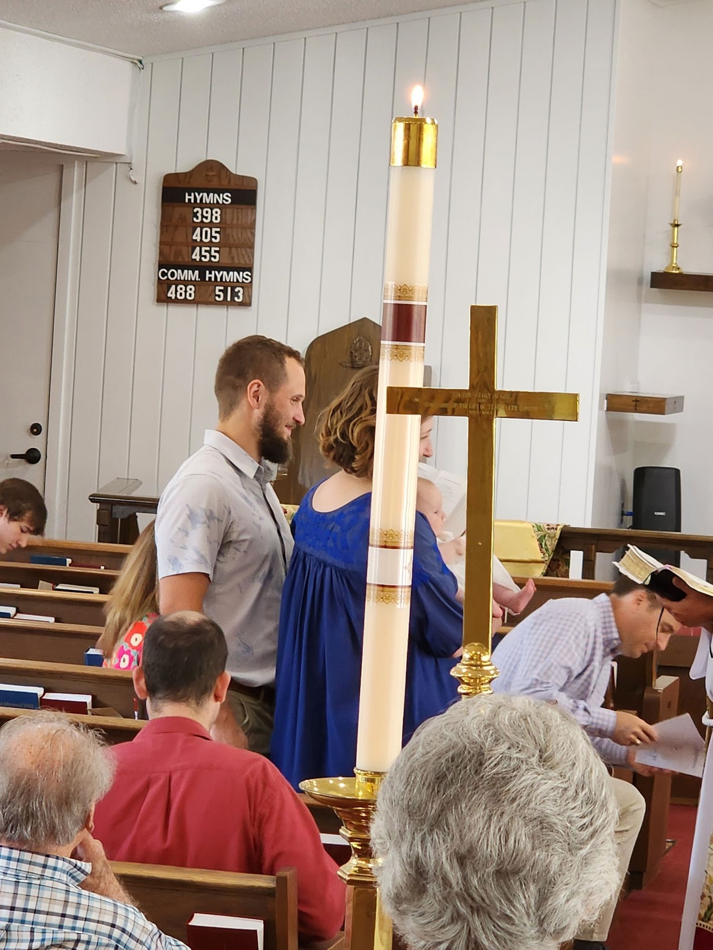Couple standing by a tall candle and cross in a church. People are in the pews.