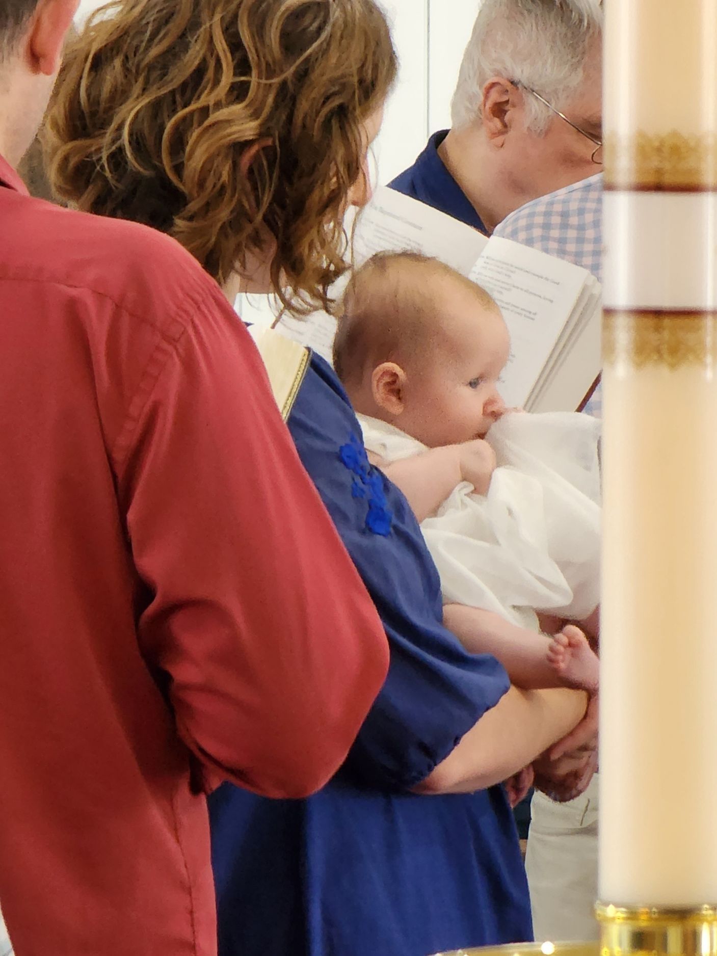 A baby in a white dress is held during a baptism ceremony.