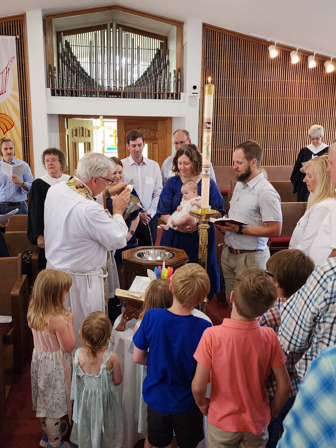 Baptism ceremony in a church with a baby, priest, and family. People are watching as the baby is baptized.