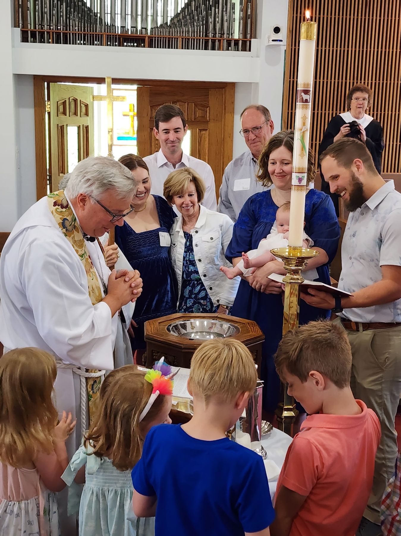 Baptism ceremony in a church: priest, baby, family, children, candle, water basin.