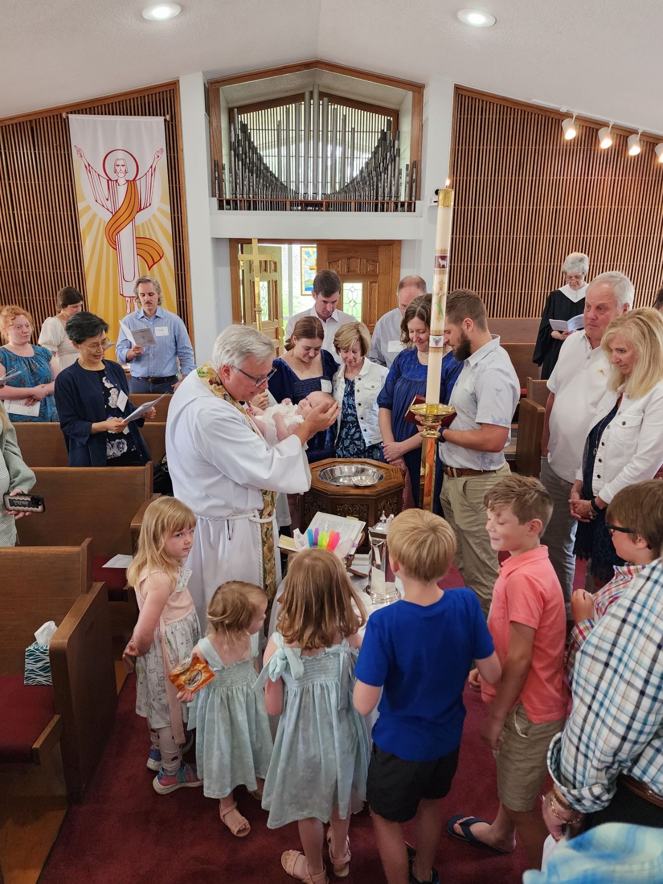 Baptism ceremony in a church. Priest holding baby, surrounded by family and children.