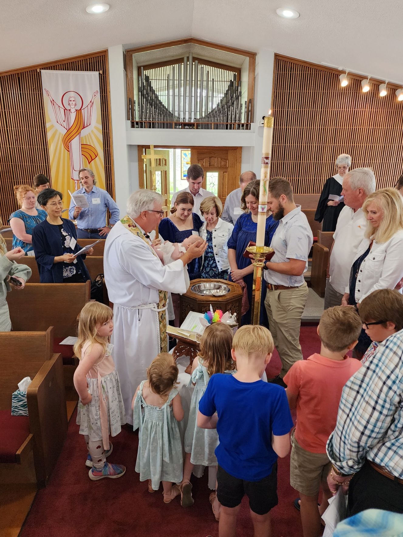 Baptism ceremony in a church: priest pouring water on a person's head, surrounded by attendees.