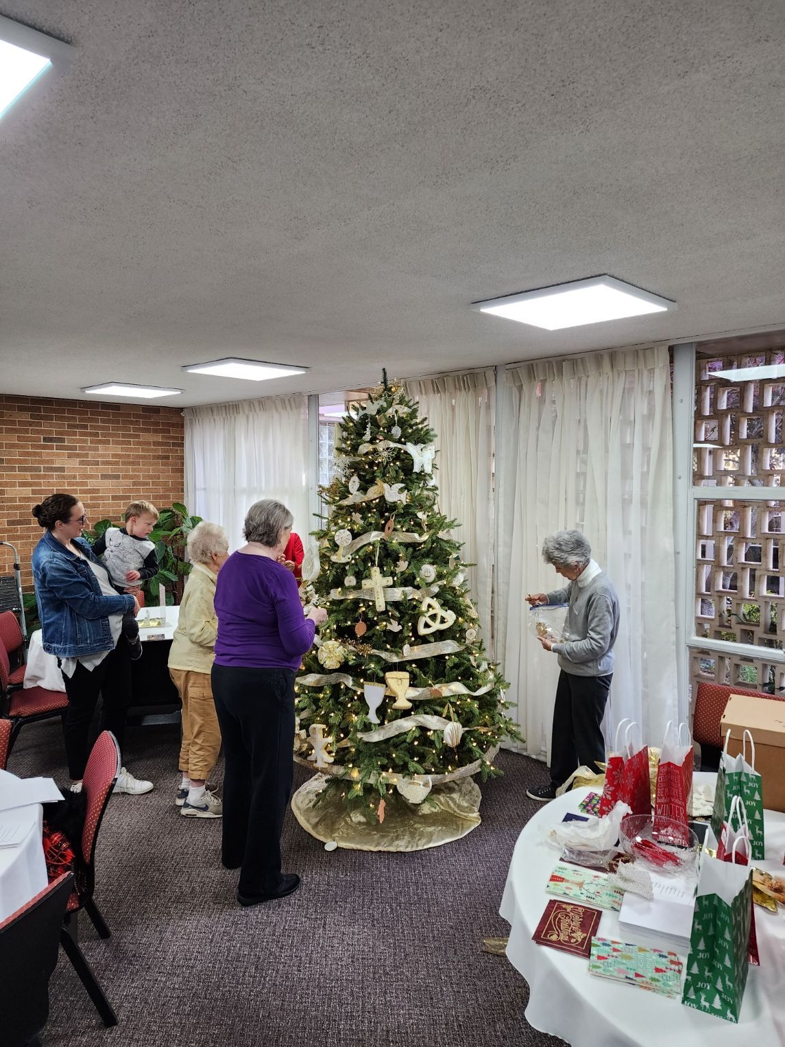 People gathered around a decorated Christmas tree in a room, examining gifts and decorations.