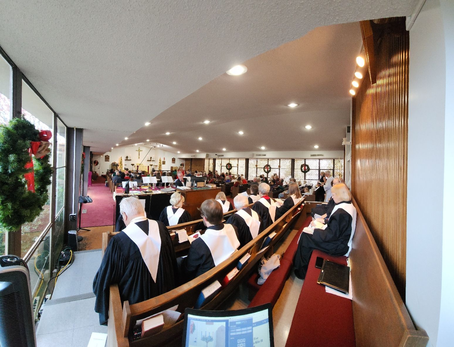 Choir members in robes singing in a church, Christmas decorations visible.