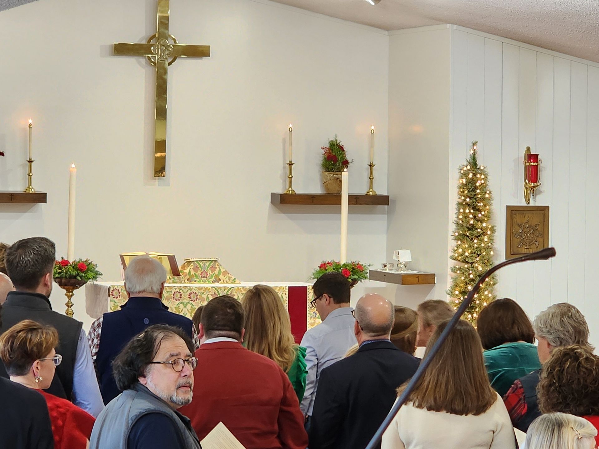 People in a church service with a cross, candles, and a Christmas tree.