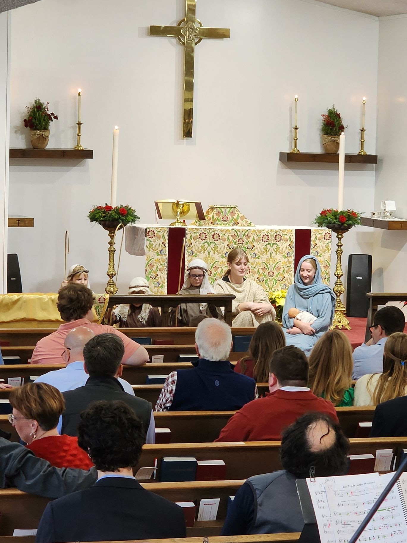 Church service with actors on stage enacting the nativity scene, audience seated.
