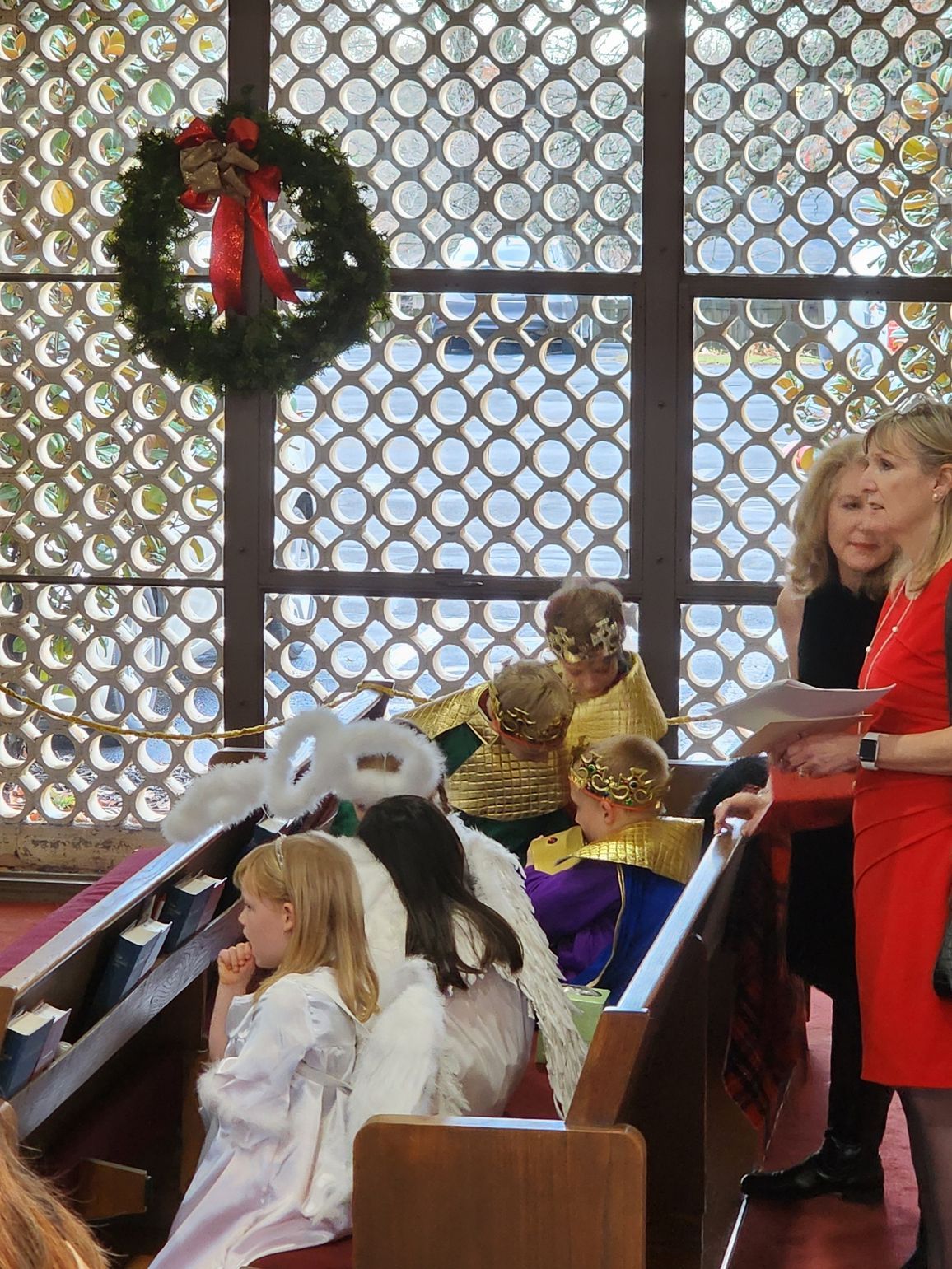 Children in costumes on church pews. Wreath in window.