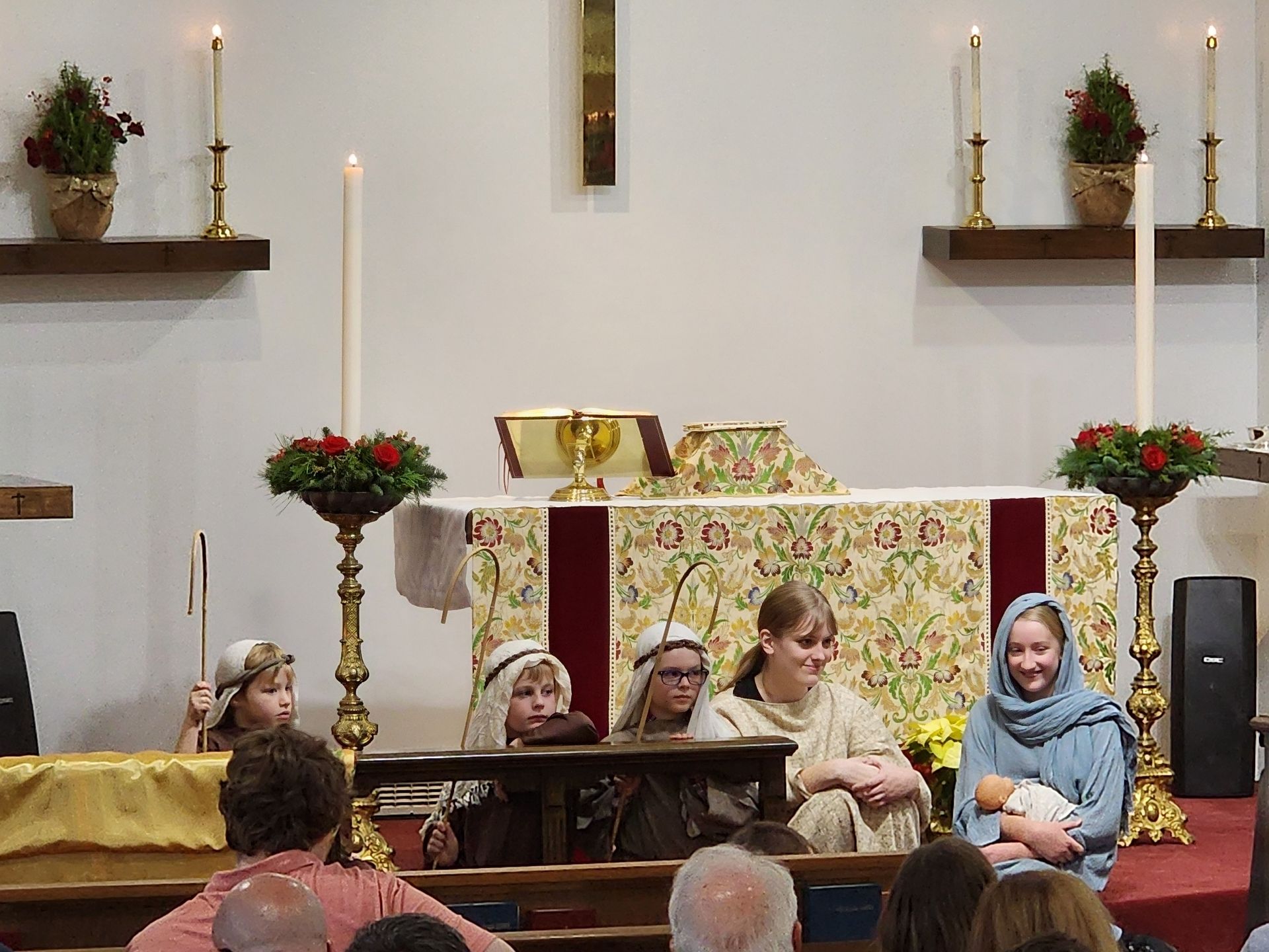 Children performing a Nativity play on a church stage; candles, decorations, costumes.