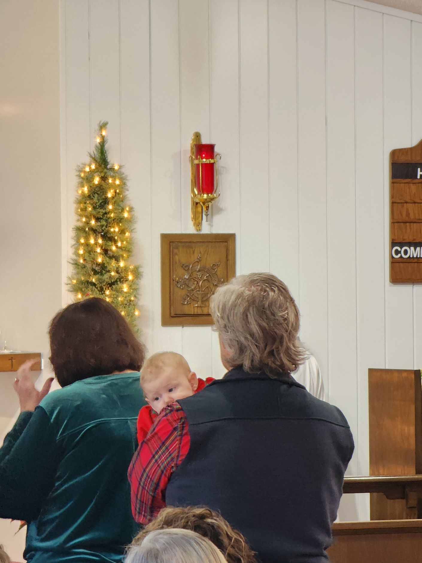 Woman holding a baby in a church, Christmas decorations on the white wall.