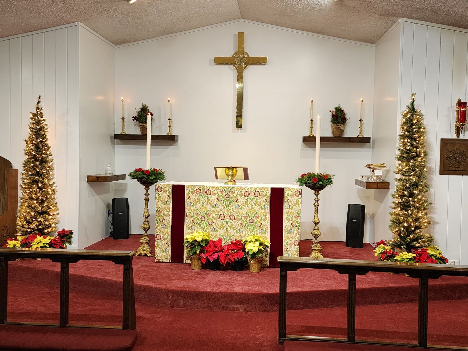 Altar in a church decorated with Christmas trees, flowers, candles, and a golden cross.