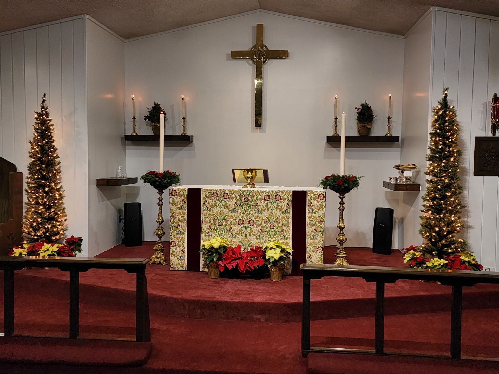 Church altar decorated for Christmas with cross, candles, and trees.