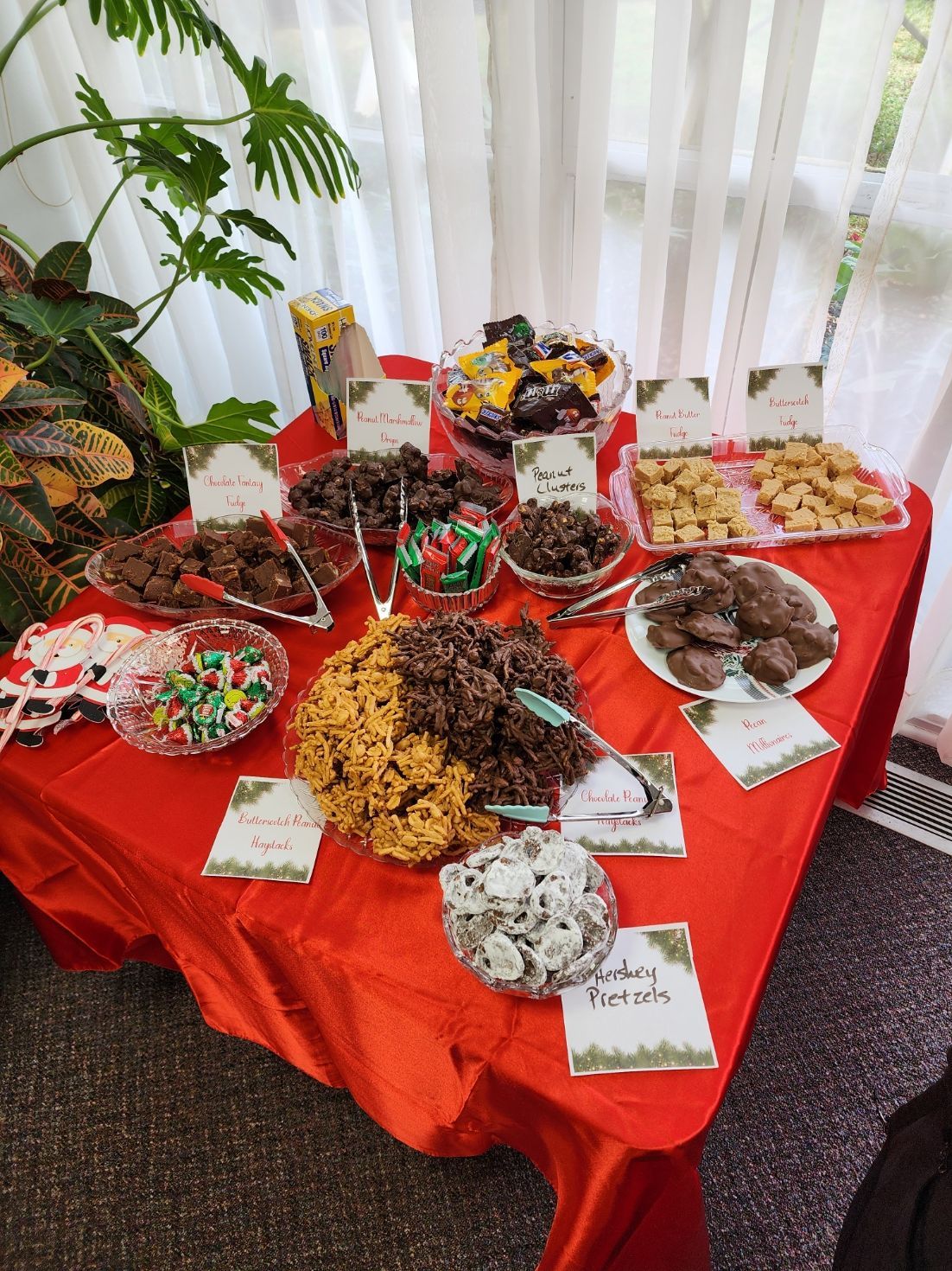 Dessert table with various candies and cookies, arranged on a red tablecloth.
