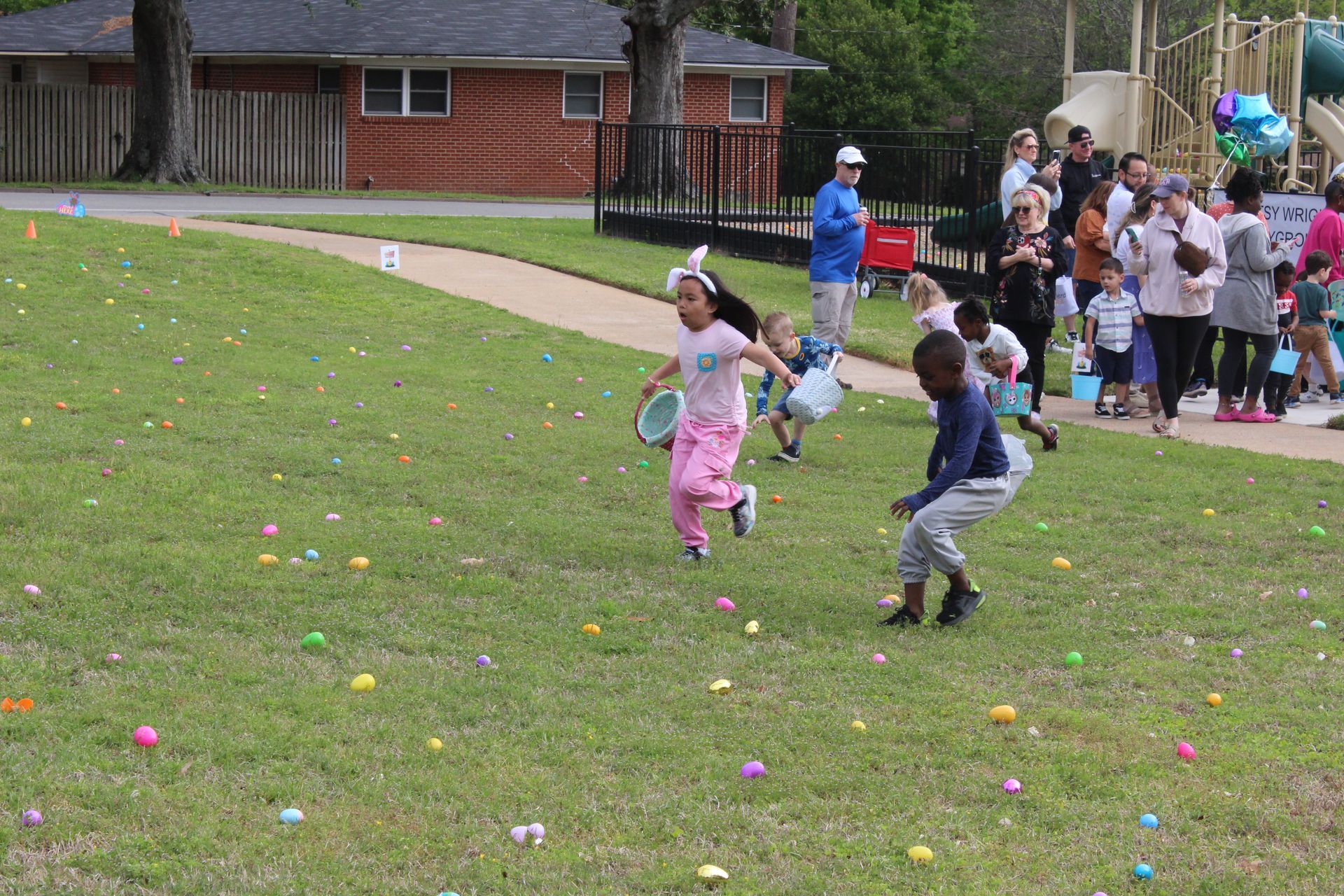 Children run on a grassy field, collecting eggs during an Easter egg hunt.