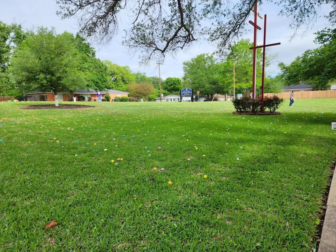 Grassy park with a large cross, trees, and a building in the background on a cloudy day.