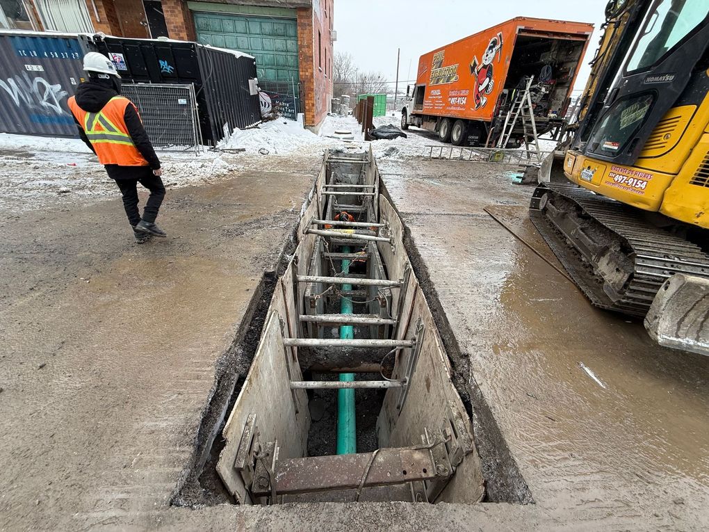 Tranchée de chantier avec des ouvriers, un camion rouge et du matériel dans une rue de la ville.