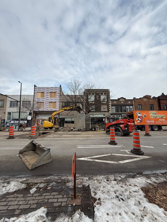 Chantier de construction avec ouvriers, camions, remorque orange et blanche, ciel couvert.