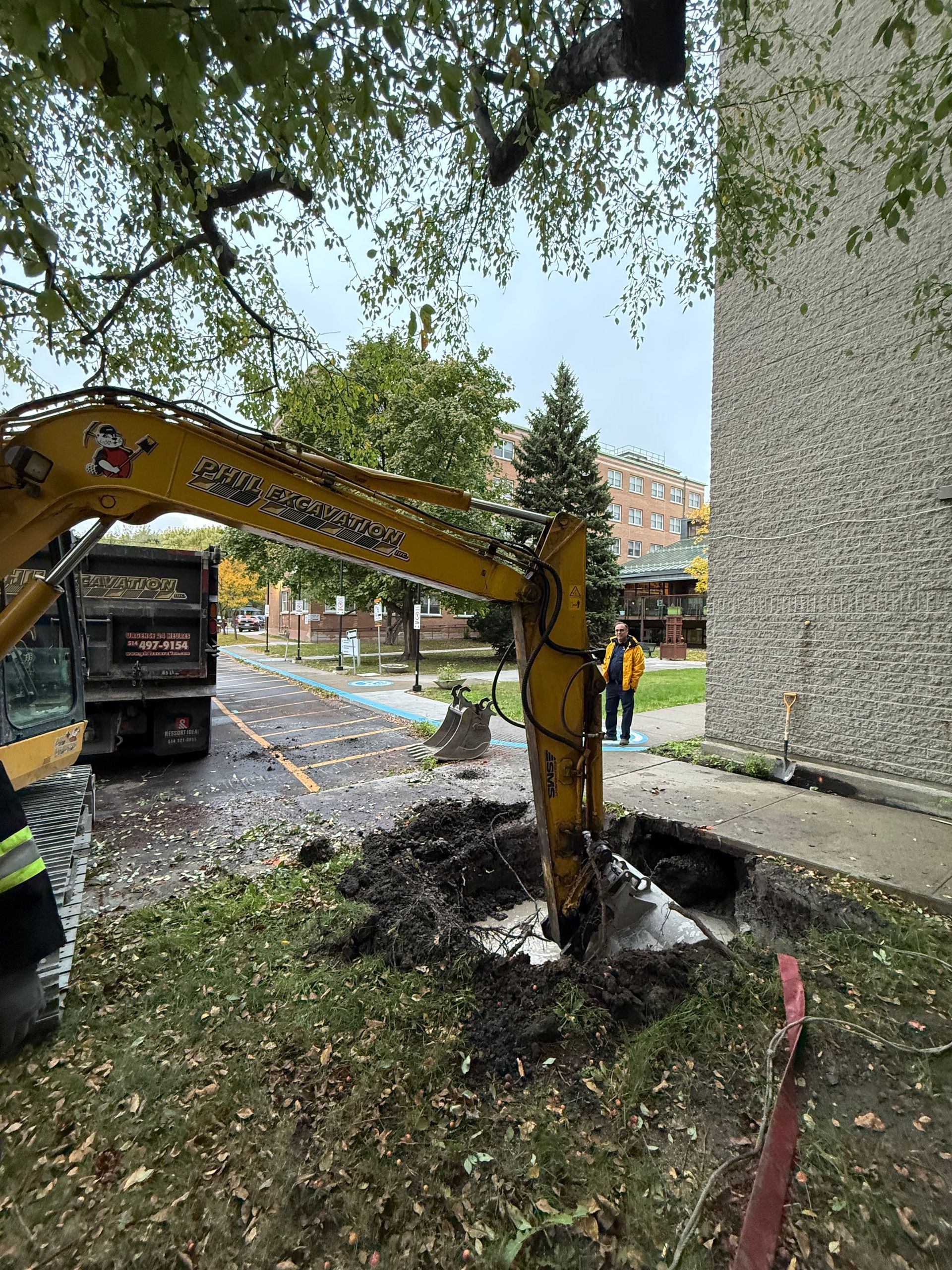 Une pelleteuse creuse près d'un bâtiment. Machine jaune, tas de terre, ouvriers qui regardent.