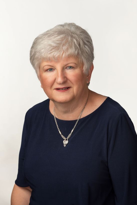 A woman is sitting at a desk with a laptop and a vase of flowers.