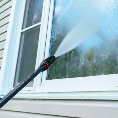 Woman in glasses and gloves cleaning a window with a yellow cloth and spray bottle.