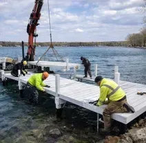 Construction crew using a crane-equipped barge to install a white modular dock into a lake.