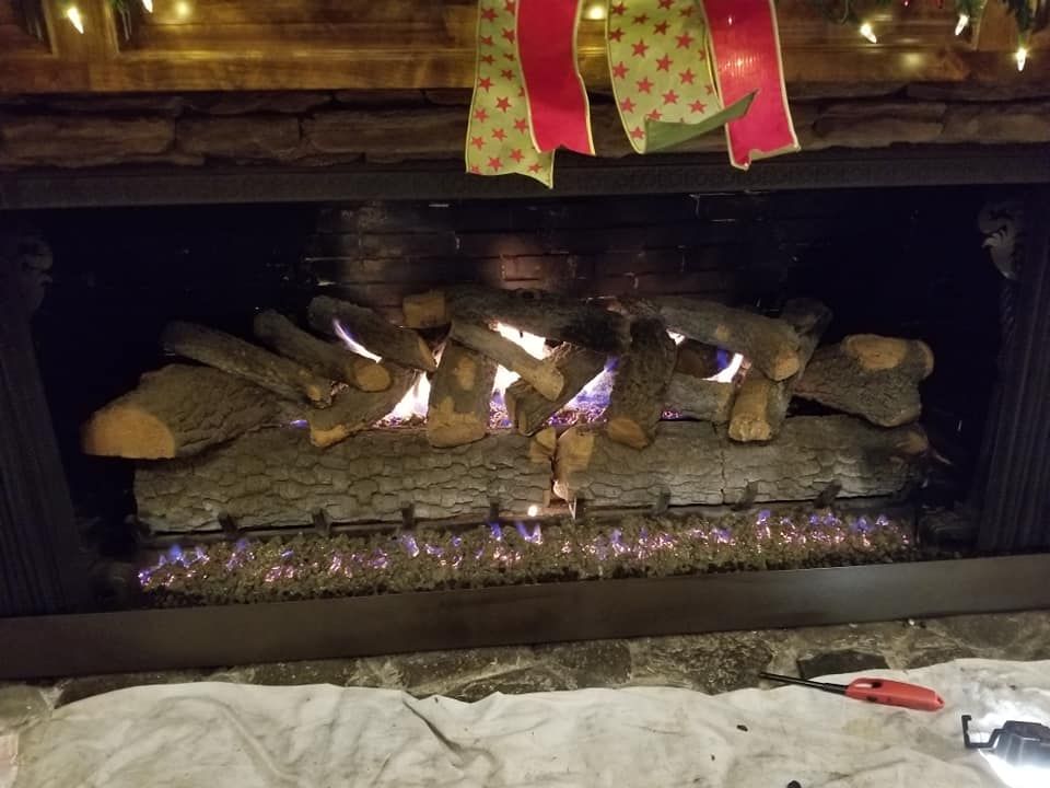 A lit fireplace with faux logs. Flames flicker below, garland and a bow are above.
