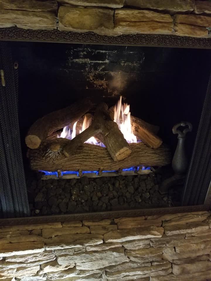 Gas fireplace with glowing blue flames and ceramic logs in a stone hearth.